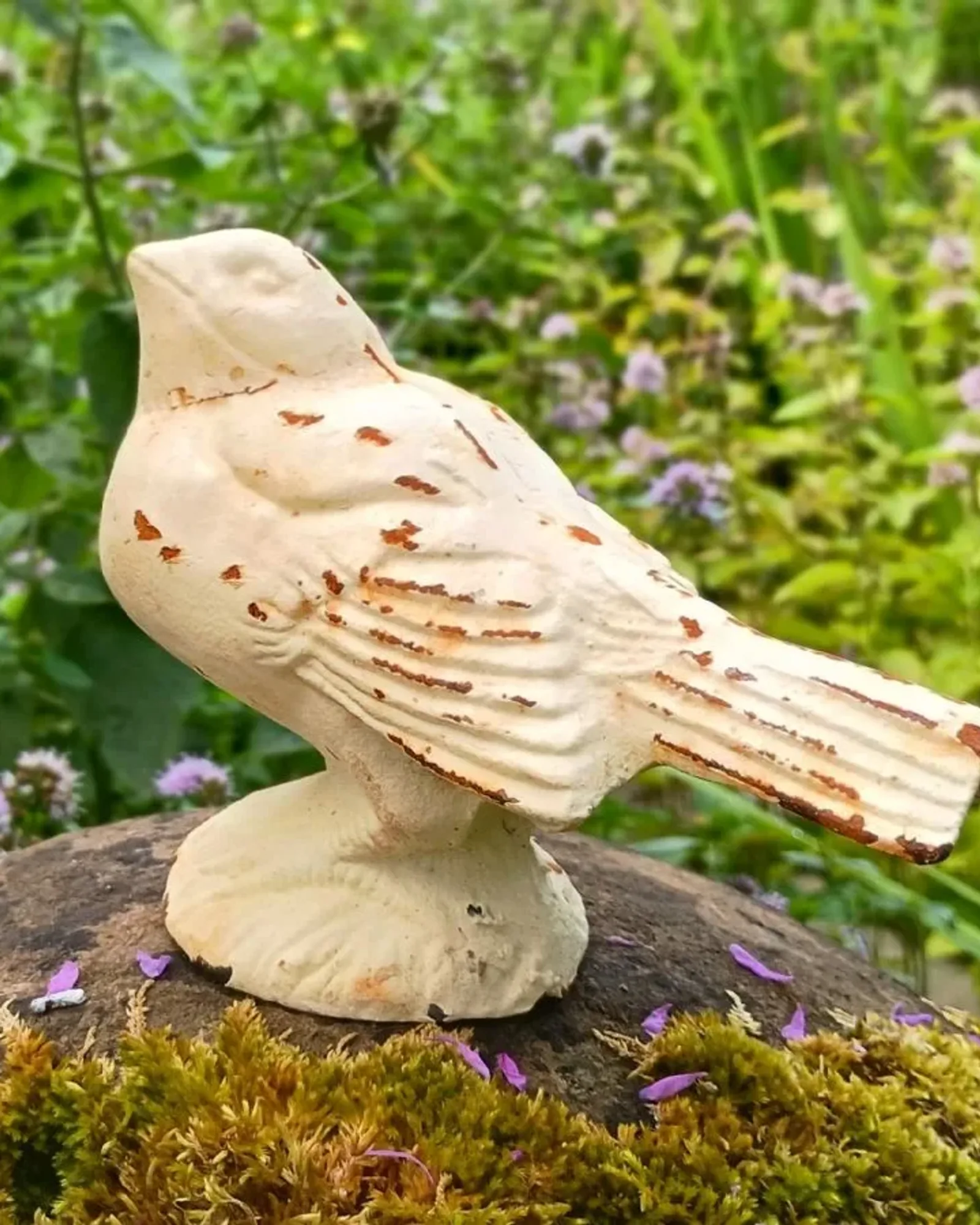 A small cast iron bird on a round base in a distressed cream paint with rust showing through.