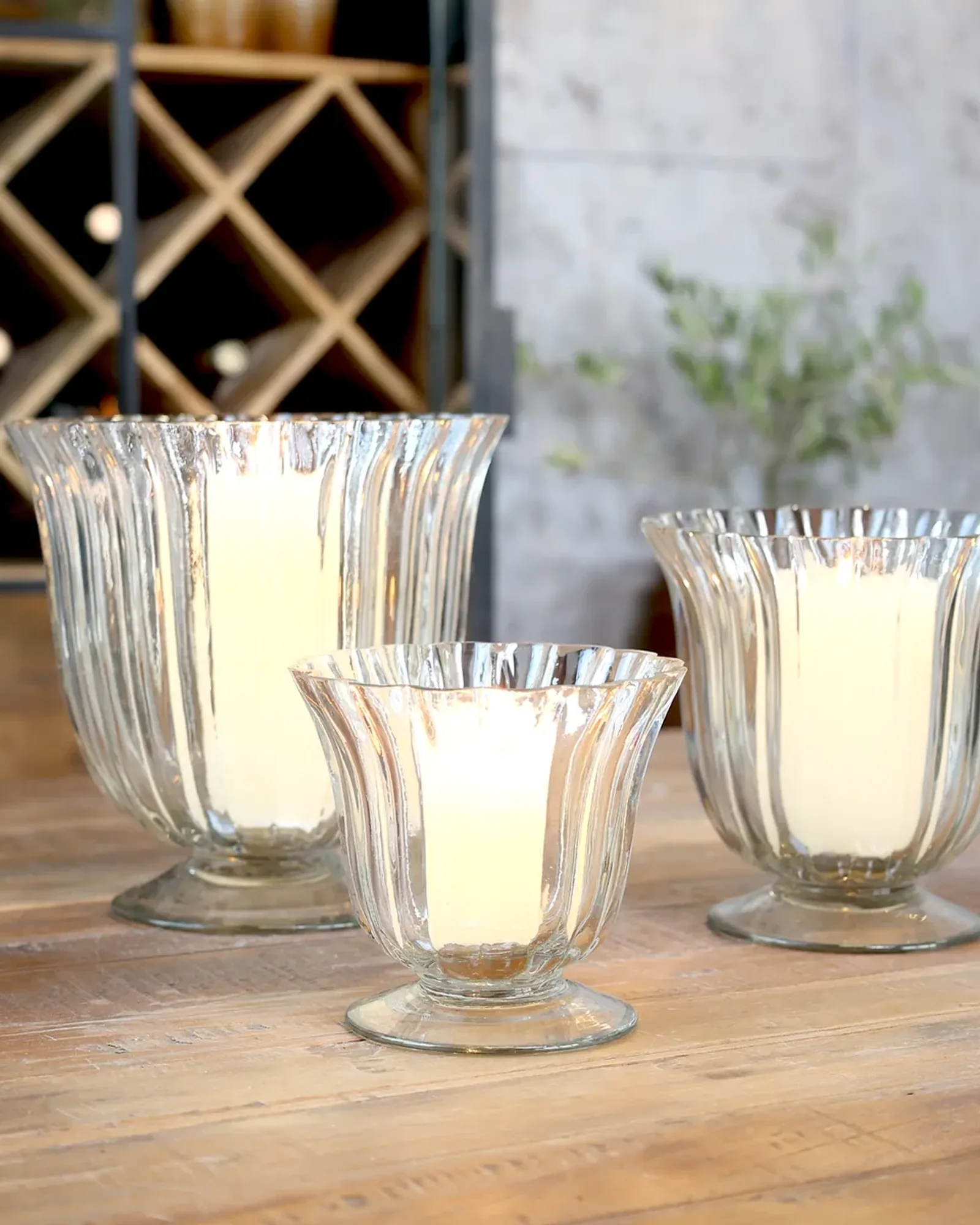 Three fluted clear-glass hurricanes on a foot in graded sizes, each with a pillar candle inside.
