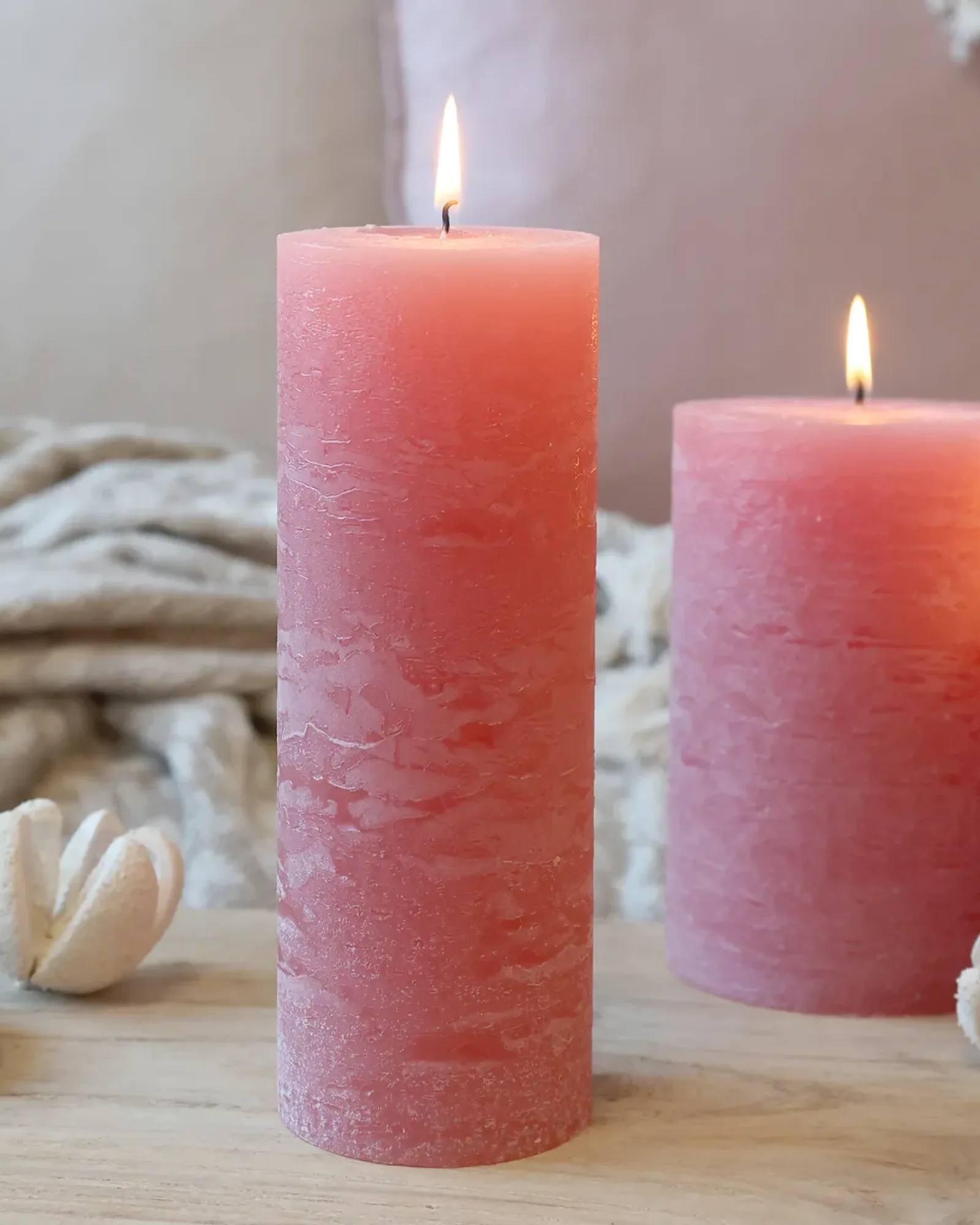 A tall, slim rustic pillar candle in raspberry pink, lit, with shorter candles of the same colour behind it.